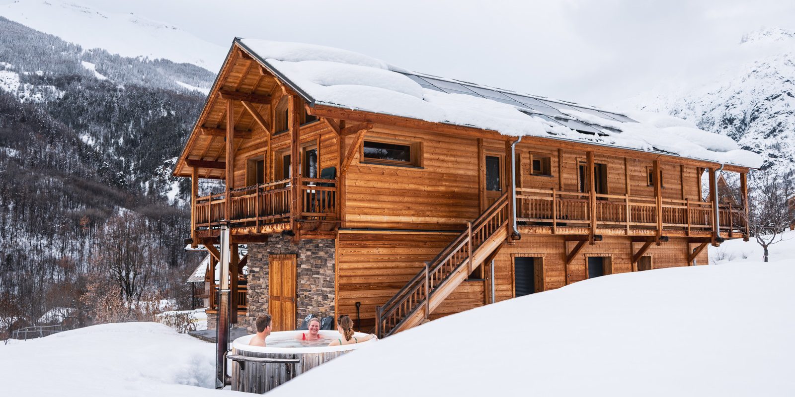 La neige recouvre le chalet mountivity, une famille se baigne dans le bain nordique sur la terrasse